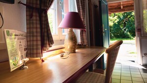 A wooden table with a lamp, a placard, and a chair in a room with plaid curtains and a view of greenery outside. - Les Loges de l'Ecomusée D'Alsace (Ungersheim)