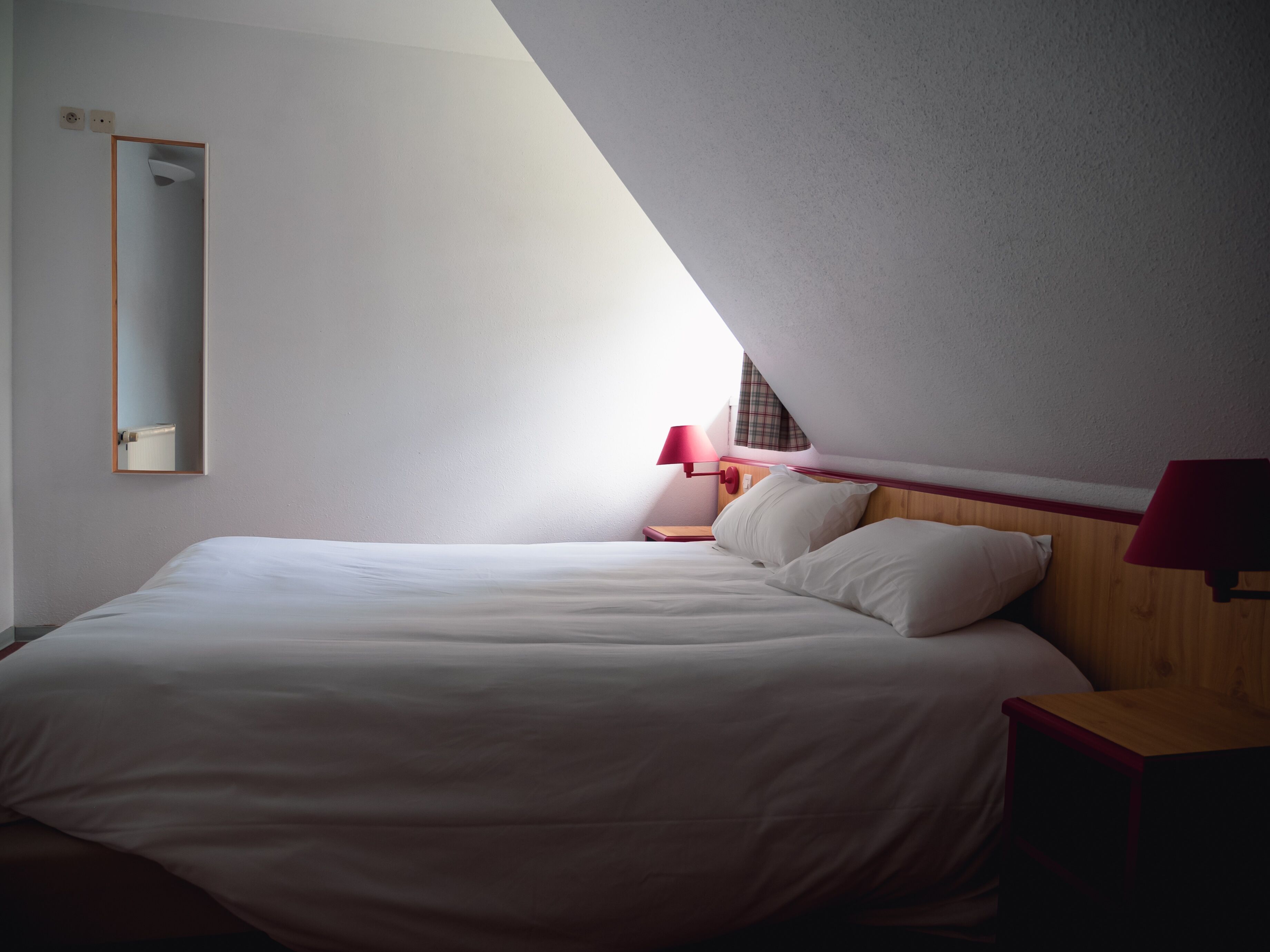 Een slaapkamer met een groot bed, een nachtkastje, een spiegel en een rode lamp.