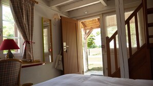 A bedroom with a bed, a chair, a lamp, a mirror, and an open door leading outside. - Les Loges de l'Ecomusée D'Alsace (Ungersheim)