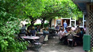An outdoor dining area with tables and chairs, surrounded by greenery and a building in the background. - Les Loges de l'Ecomusée D'Alsace (Ungersheim)