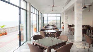 A spacious outdoor dining area with large windows, wicker furniture, and ceiling fans. - Villas Buenavista (San Juan)
