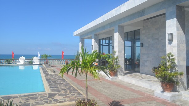 A pool area with a clear view of the ocean, a modern building with large windows, and potted plants. - Villas Buenavista (San Juan)