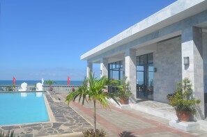 A pool area with a clear view of the ocean, a modern building with large windows, and potted plants. - Villas Buenavista (San Juan)