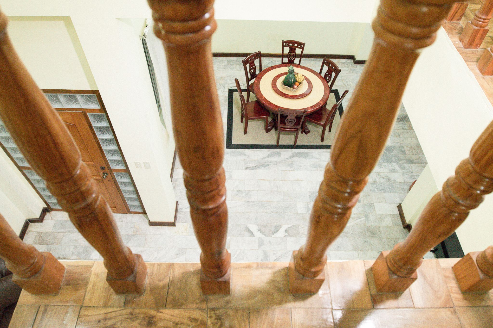 Un coin repas avec une table ronde et des chaises, un escalier avec des balustrades en bois et un sol à motifs.