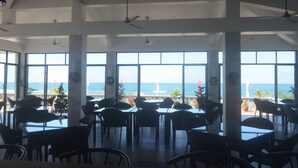 A spacious indoor area with large windows offering a view of the ocean. There are multiple tables and chairs arranged for dining or sitting. - Villas Buenavista (San Juan)