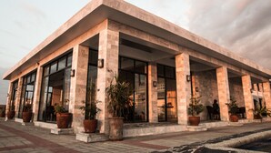 A modern building with large glass windows and columns, featuring outdoor seating and potted plants. - Villas Buenavista (San Juan)