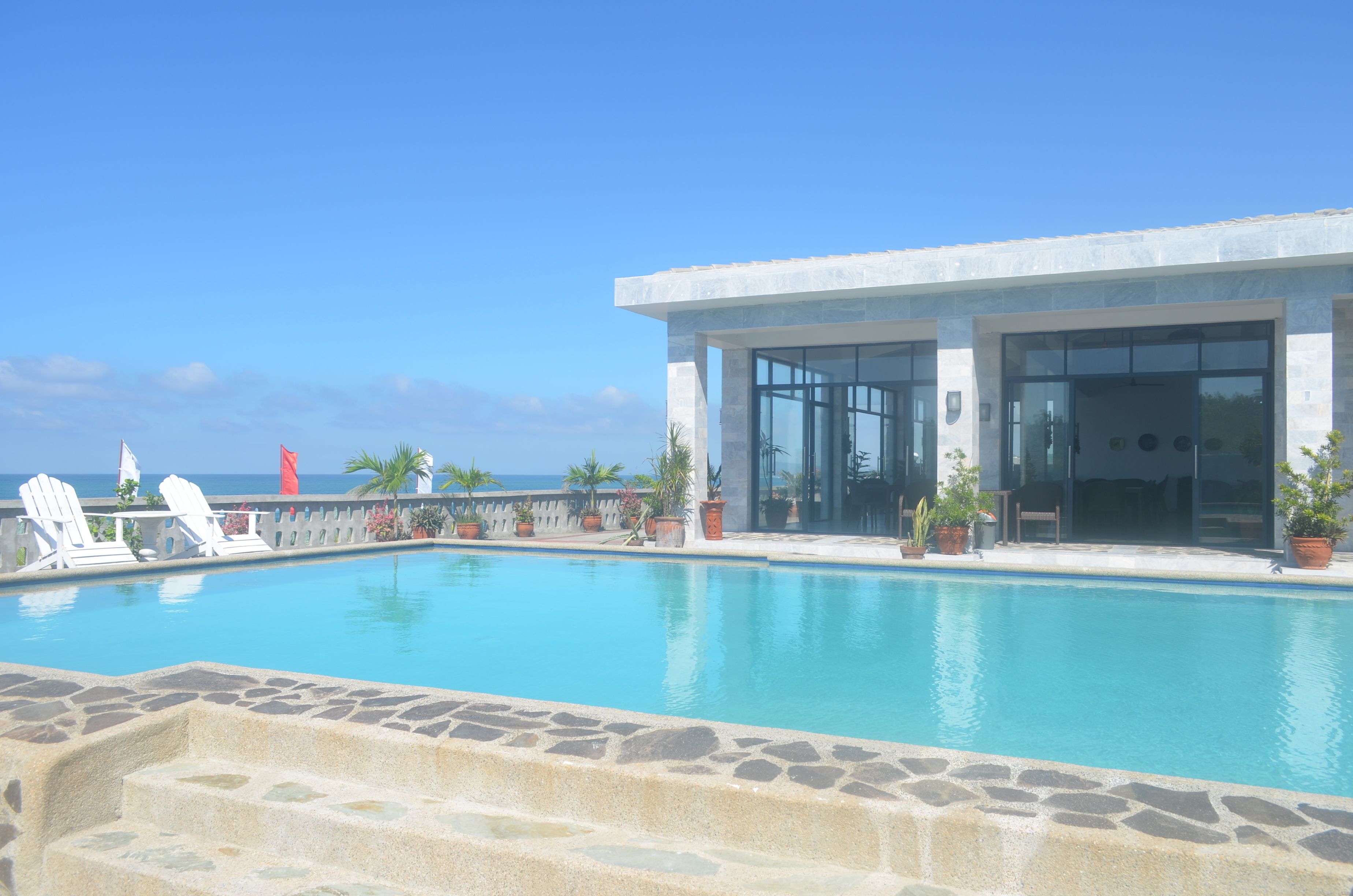 A modern pool area with clear blue water, lounge chairs, and potted plants.