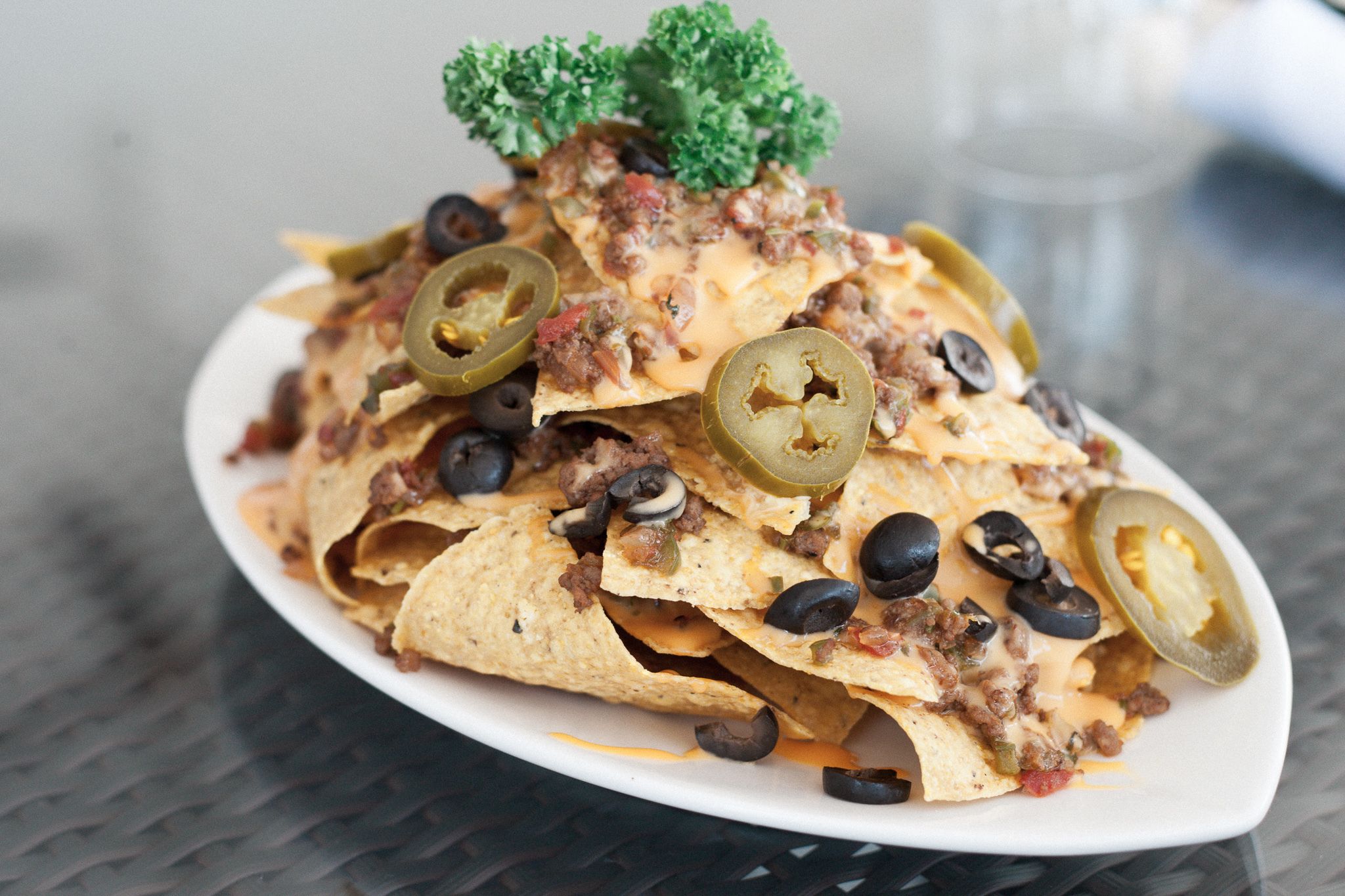 Nachos cubiertos de carne molida, queso, jalapeños y aceitunas negras sobre un plato blanco.