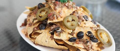 Nachos cubiertos de carne molida, queso, jalapeños y aceitunas negras sobre un plato blanco.