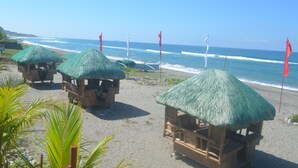 Thatched-roof huts on a beach with the ocean in the background. - Villas Buenavista (San Juan)
