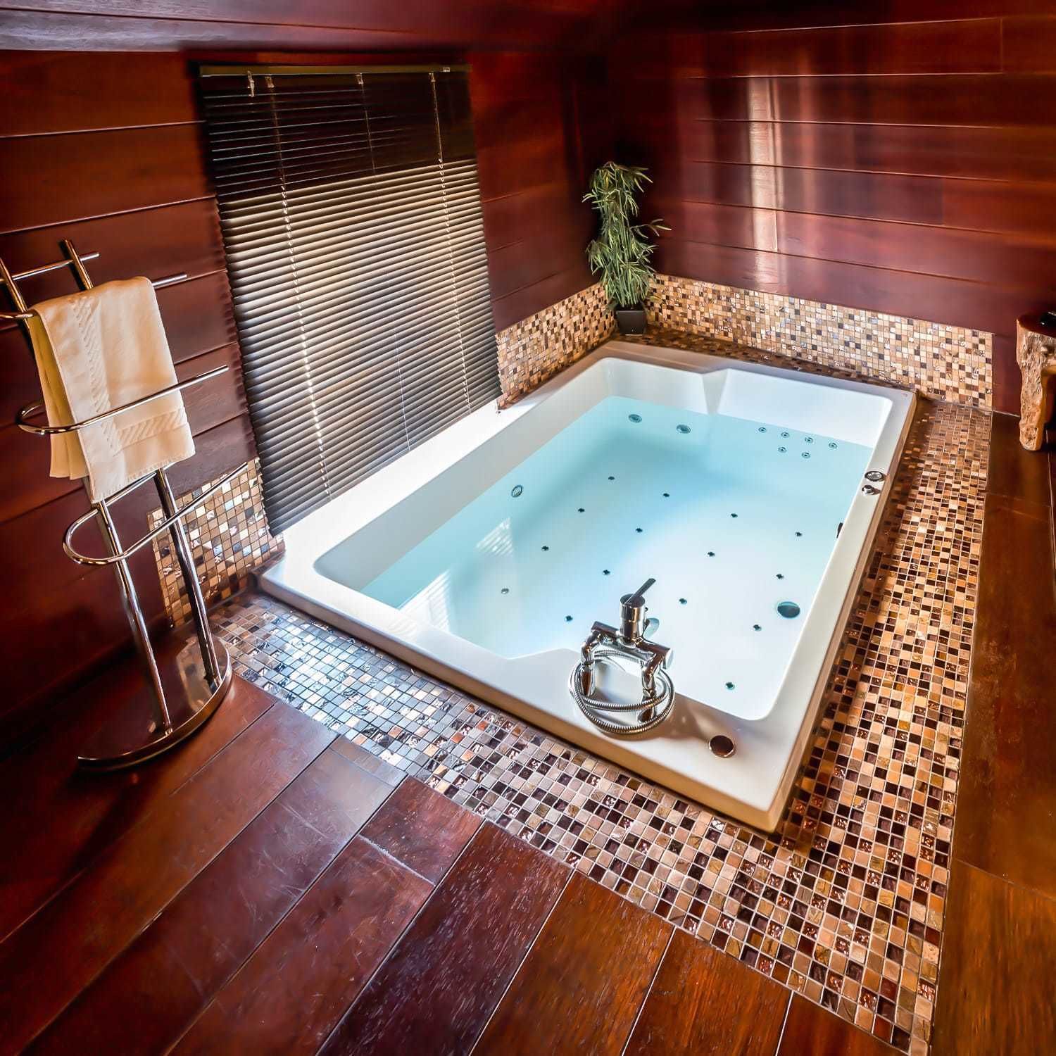 A large, square hot tub with a chrome faucet, surrounded by a mosaic tile border.