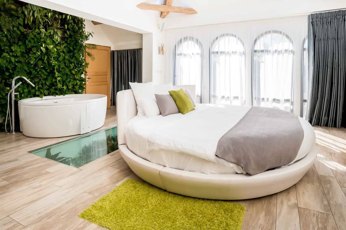 A modern bedroom with a circular bed, a jacuzzi, and a glass-enclosed pool.