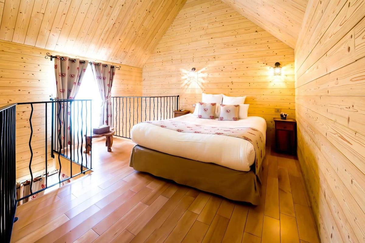 A cozy wooden cabin bedroom with a large bed, a small bedside table, and a window with curtains.