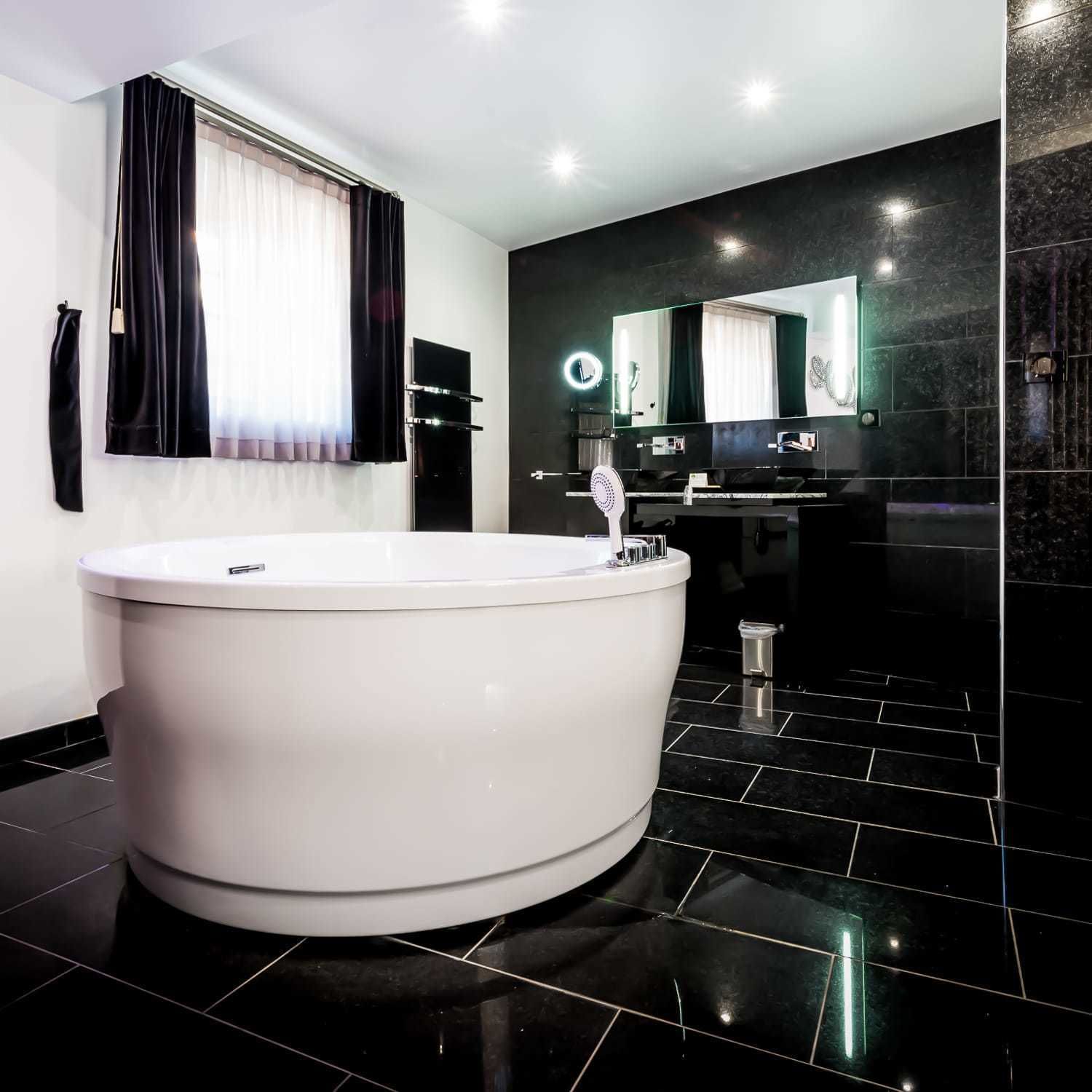 A modern bathroom with a freestanding bathtub, a vanity with a mirror, and black tiled flooring.