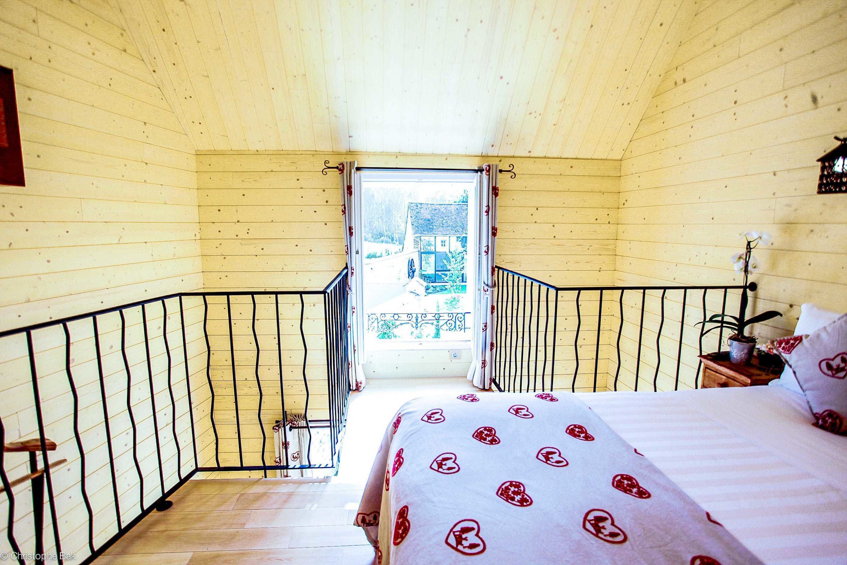 A bedroom with a bed, a nightstand, a window, and a balcony.