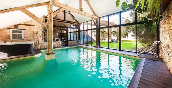 Una piscina interior con solárium de madera, paredes de piedra y amplios ventanales.