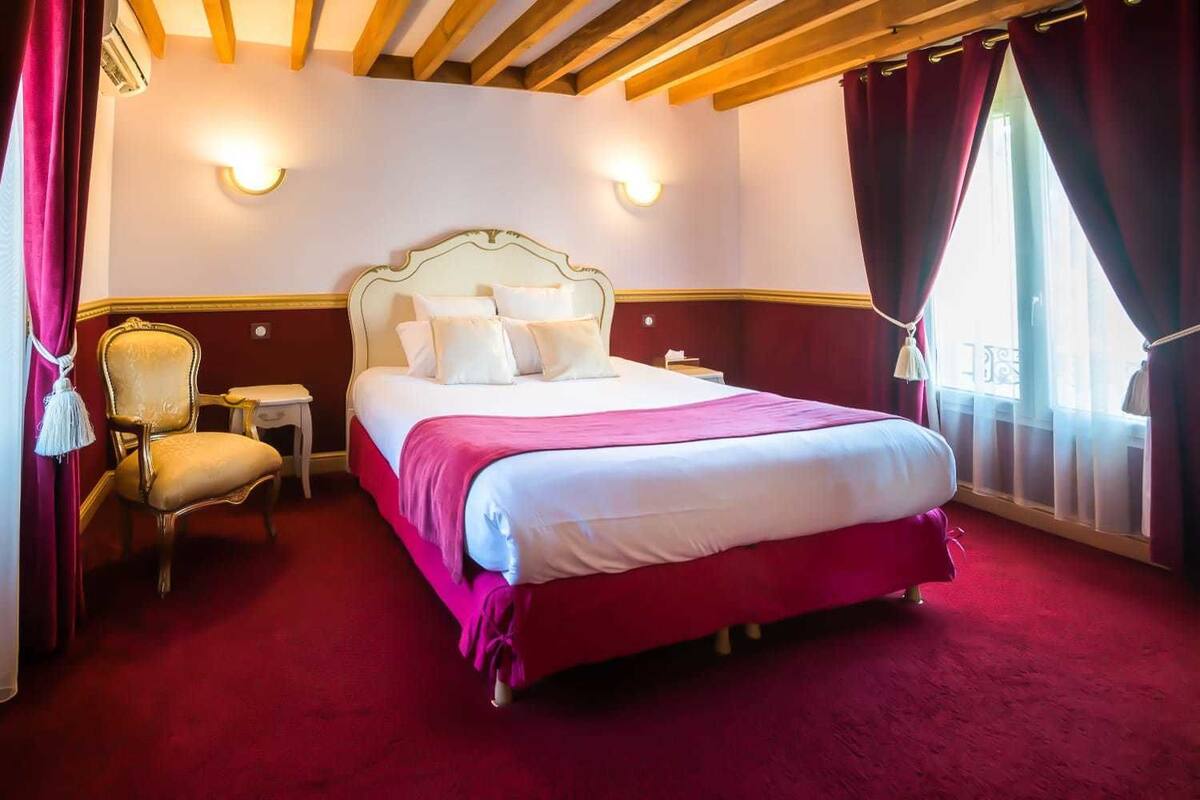 A hotel room with a large bed, a chair, a nightstand, and a window with curtains.