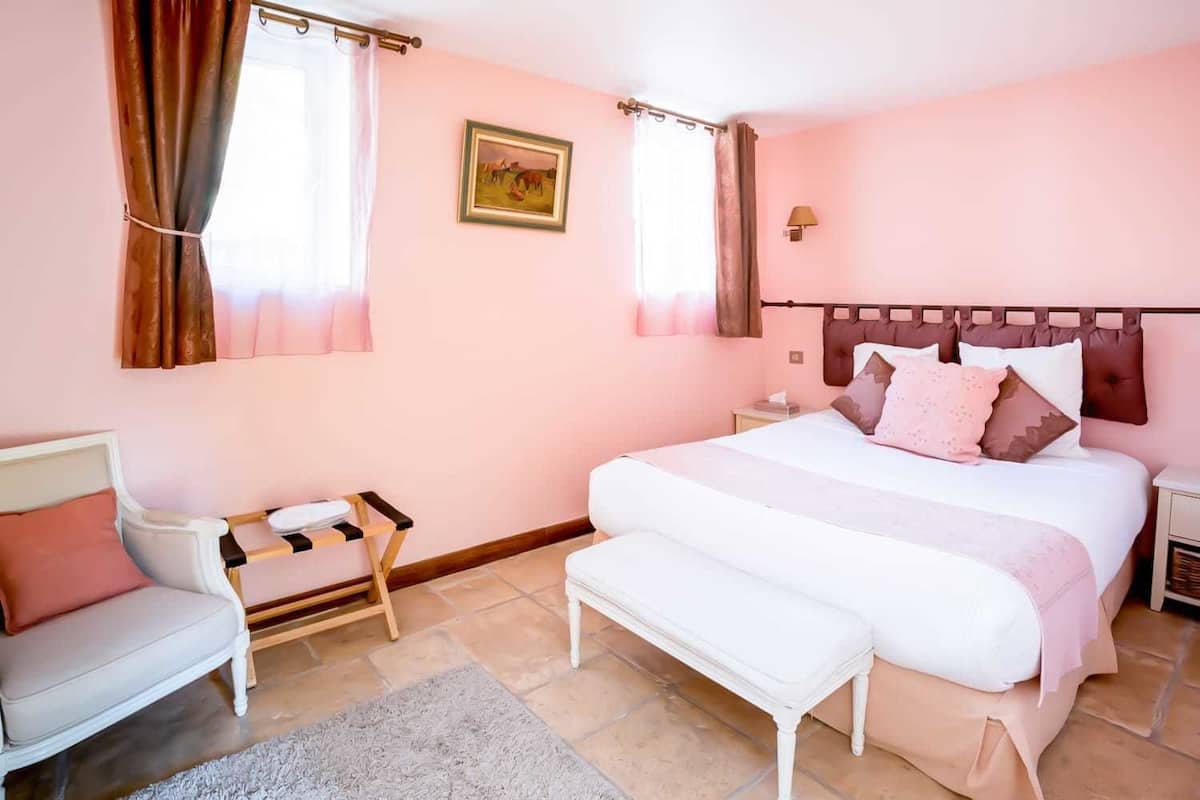 A bedroom with a large bed, a bedside table, a chair, and a window with curtains.
