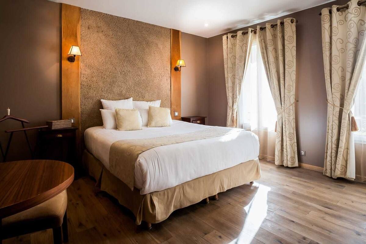 A neatly arranged hotel room with a large bed, two bedside tables, a wooden chair, and a round table.