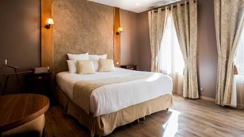 A neatly arranged hotel room with a large bed, two bedside tables, a wooden chair, and a round table.