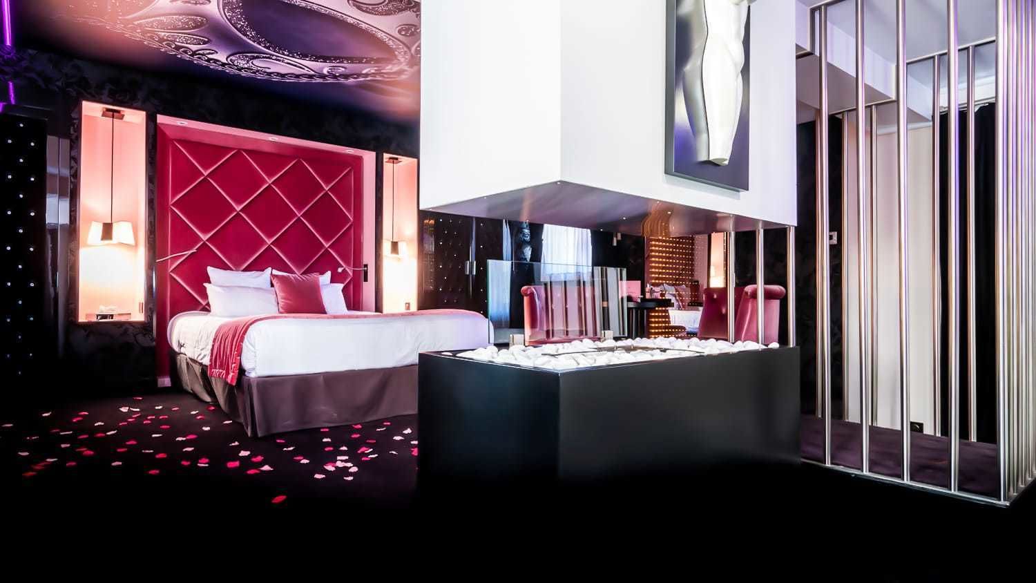 A modern hotel room with a large bed, a red accent wall, a glass partition, and a decorative centerpiece.