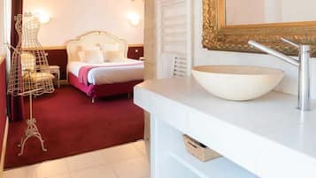Habitación de hotel con una cama grande, un tocador blanco con lavabo, un espejo con marco dorado y vigas de madera a la vista en el techo.