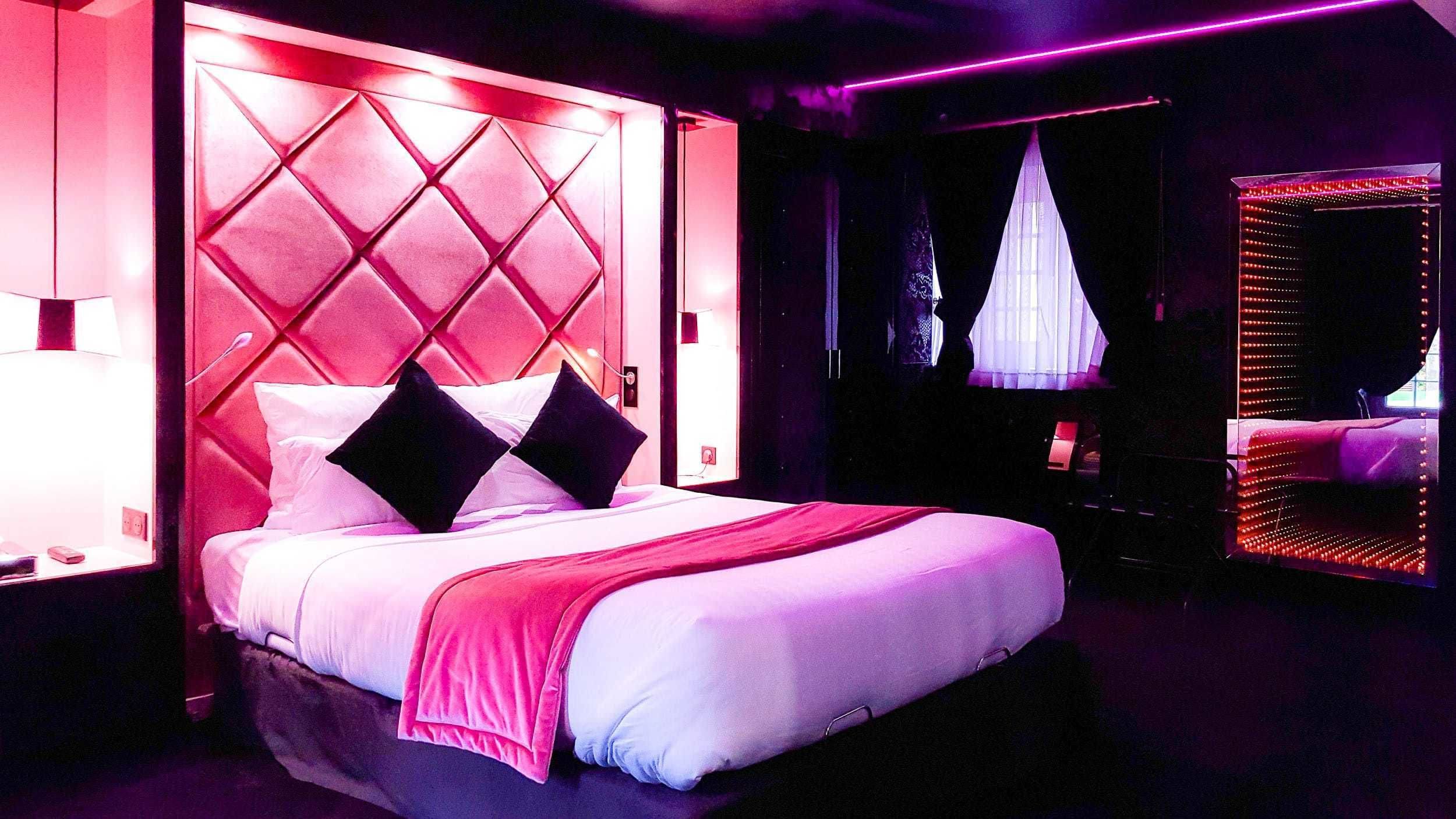 A modern hotel room with a large bed, a decorative headboard, and ambient lighting.