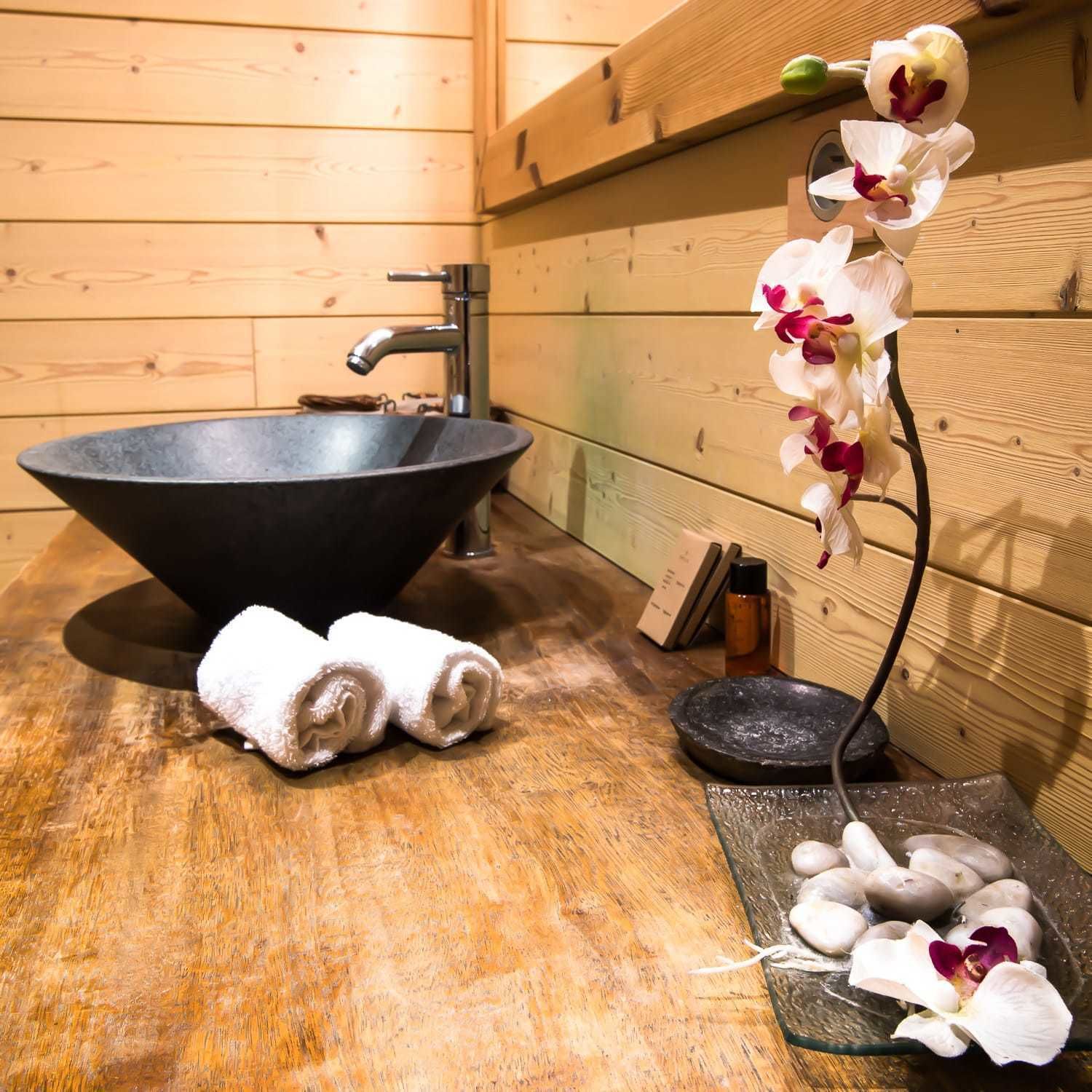 A wooden interior with a black bowl sink, a towel, and a flower arrangement.