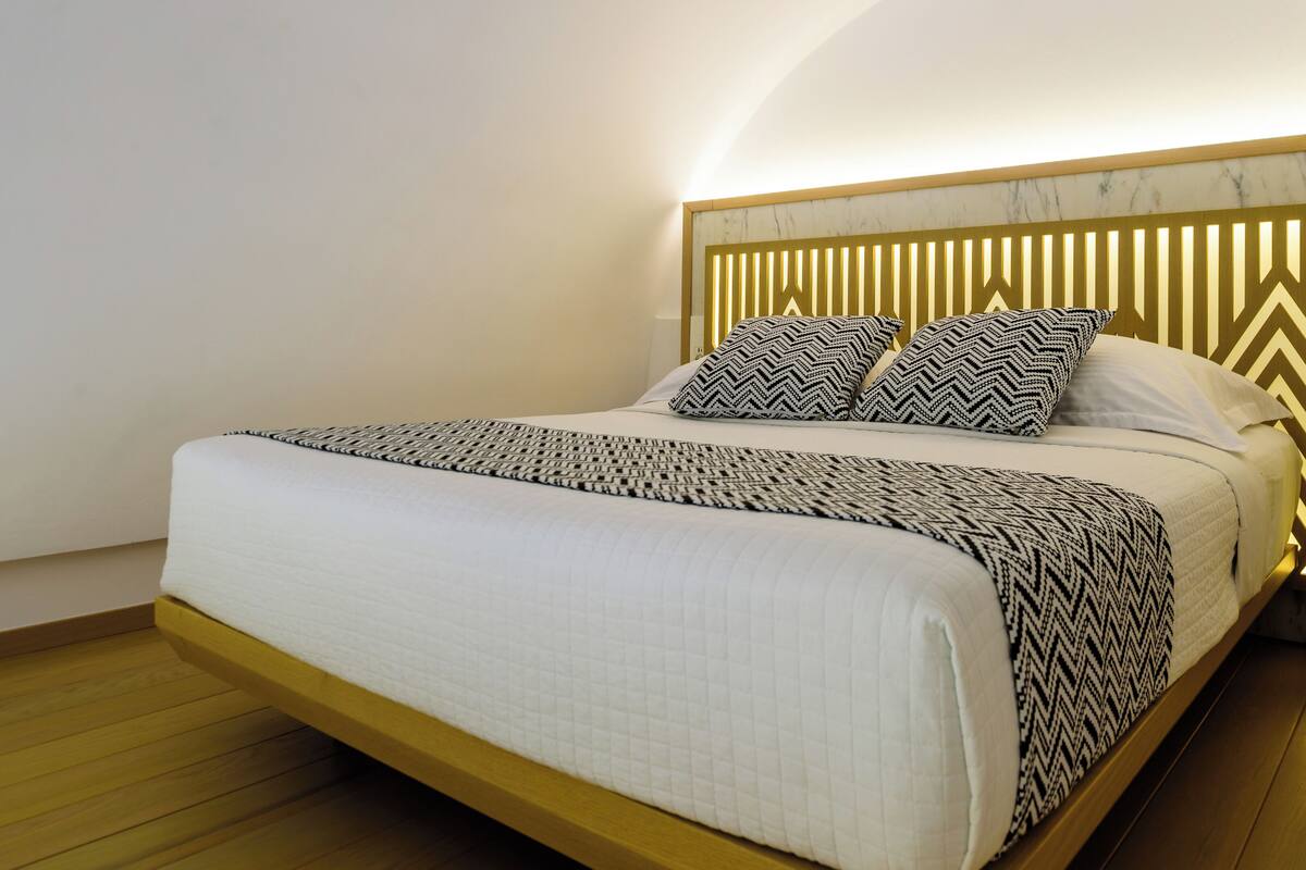 A modern bedroom with a wooden bed frame, a white quilted bedspread, and patterned pillows.