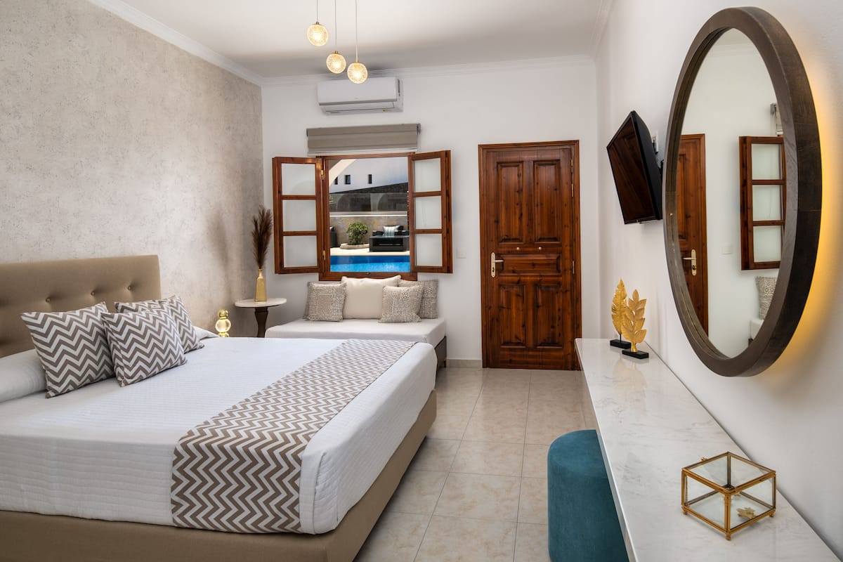 A bedroom with a large bed, a bedside table, a mirror, and a view of a pool through an open door.