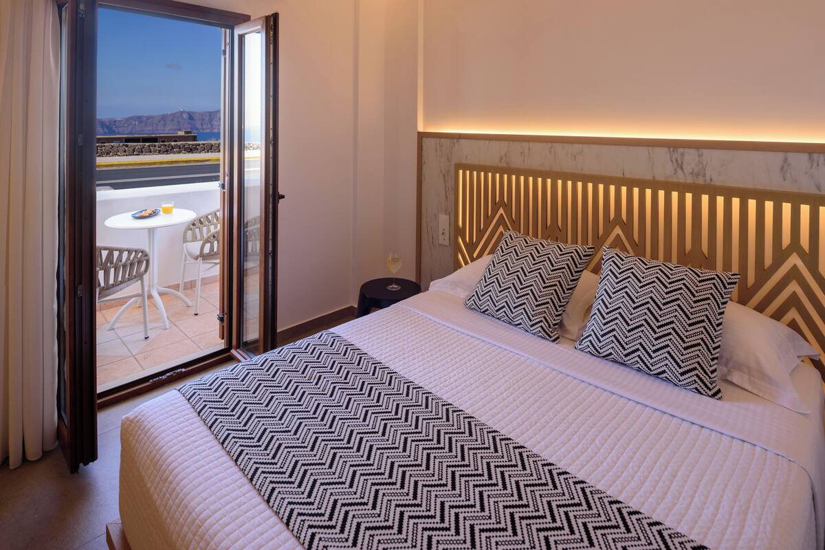 A hotel room with a bed, a bedside table, a chair, and a view of the outside.