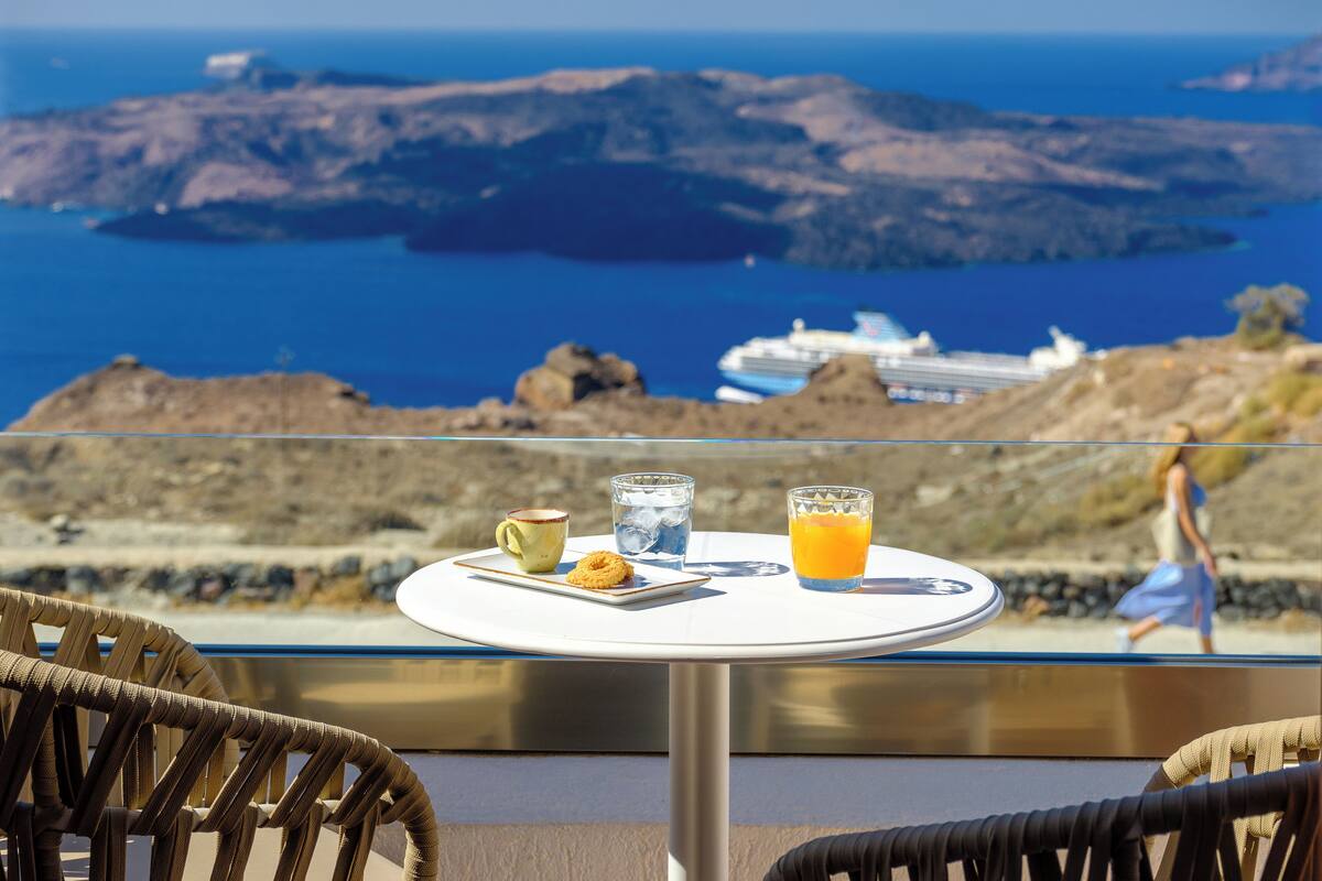 A table with a meal and drinks, overlooking a scenic view of the sea and islands.