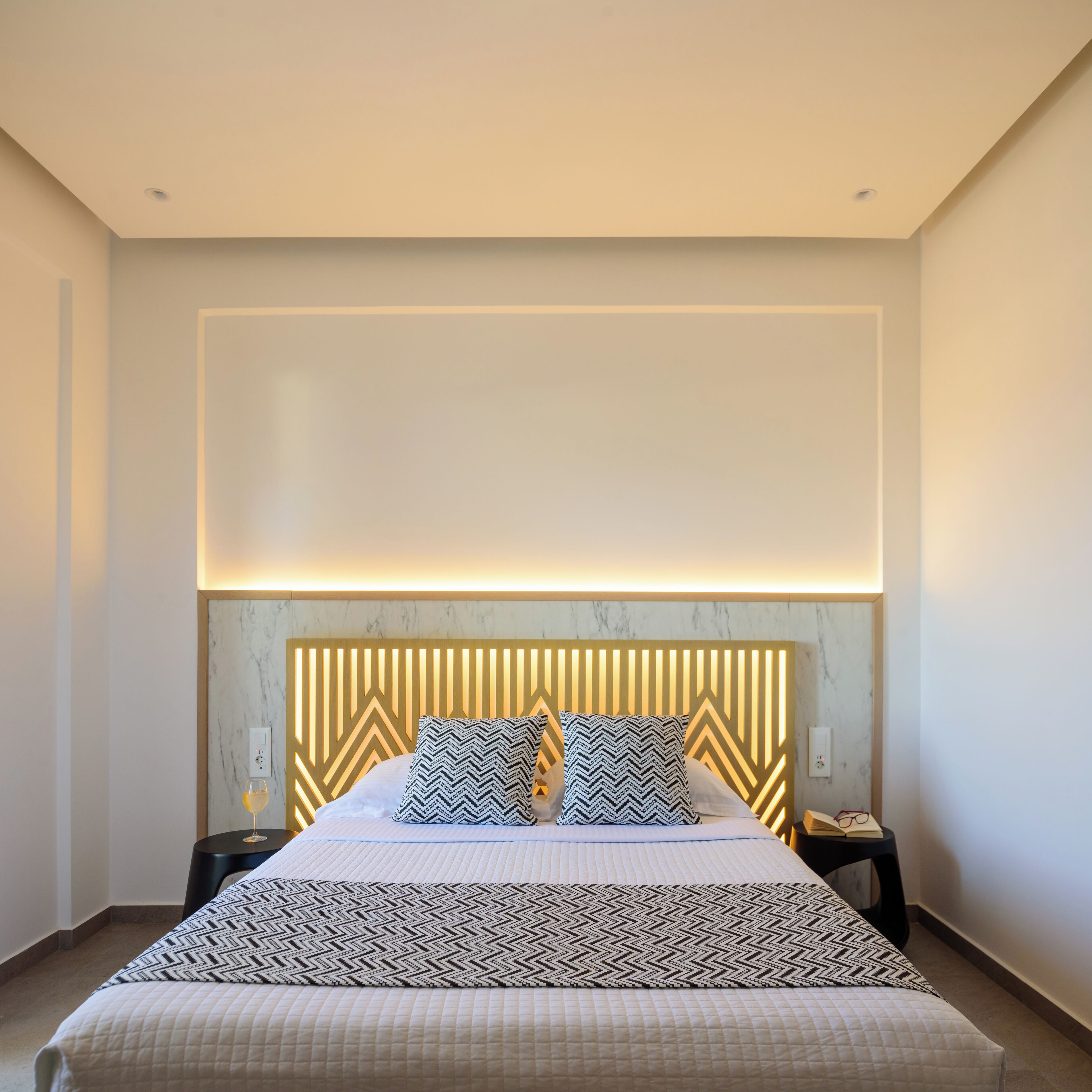 A modern hotel room with a large bed, a marble headboard, and a geometric-patterned throw blanket.