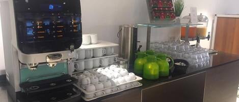 A coffee station with a coffee machine, cups, and a glass display case with condiments.