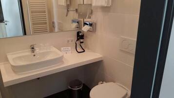 Un baño con lavamanos blanco, espejo, dispensador de toallas y retrete.