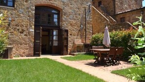 A stone building with a large arched doorway, a patio with a table and chairs, and a stone wall. - Antico Borgo Casalappi (Campiglia Marittima)
