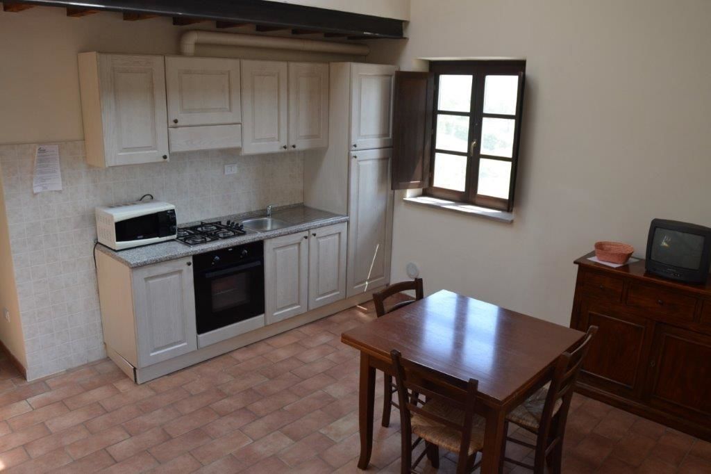 A compact kitchen with white cabinets, a gas stove, a microwave, and a small dining table with chairs.