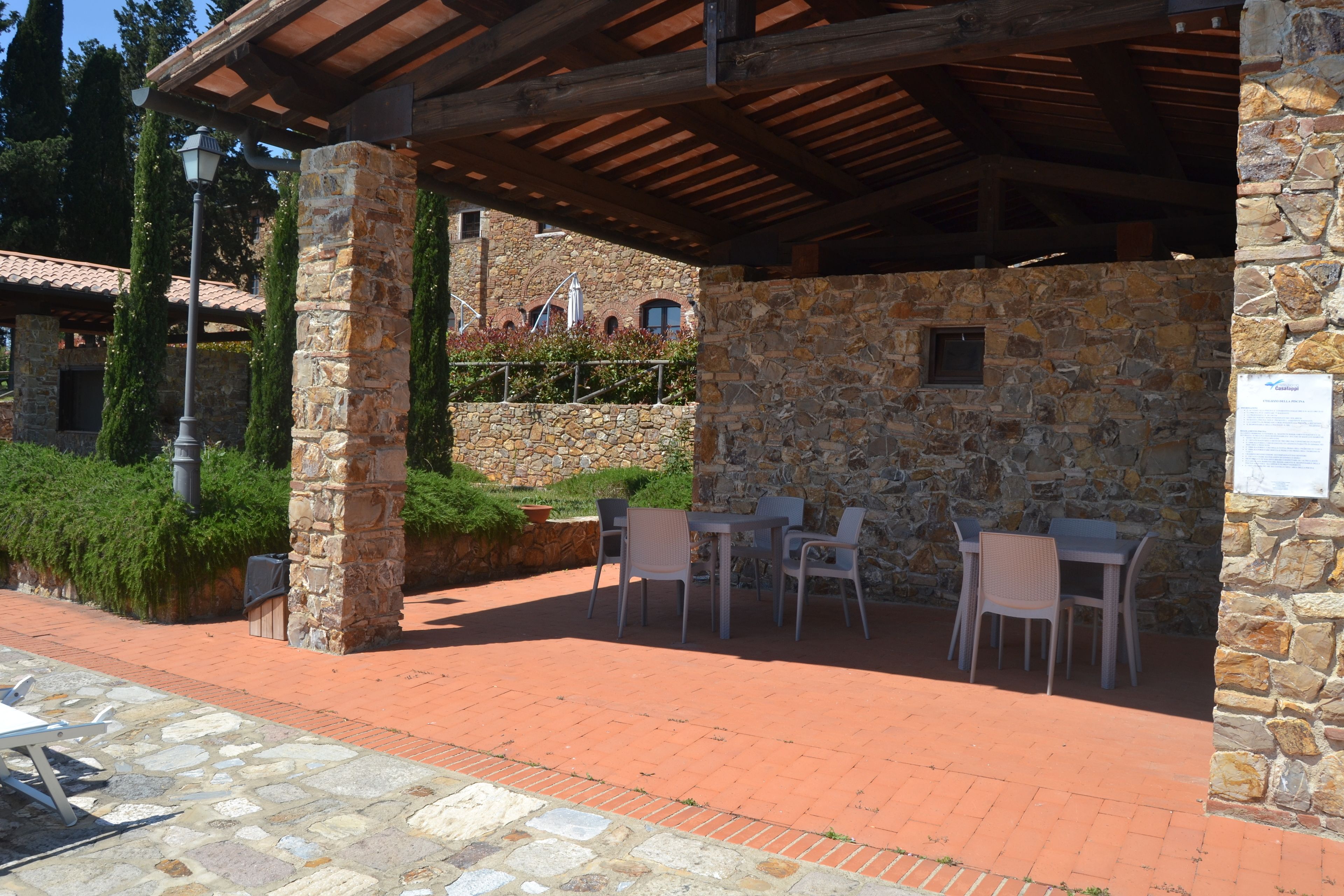 An outdoor patio with stone walls, a covered seating area, and a stone building in the background.