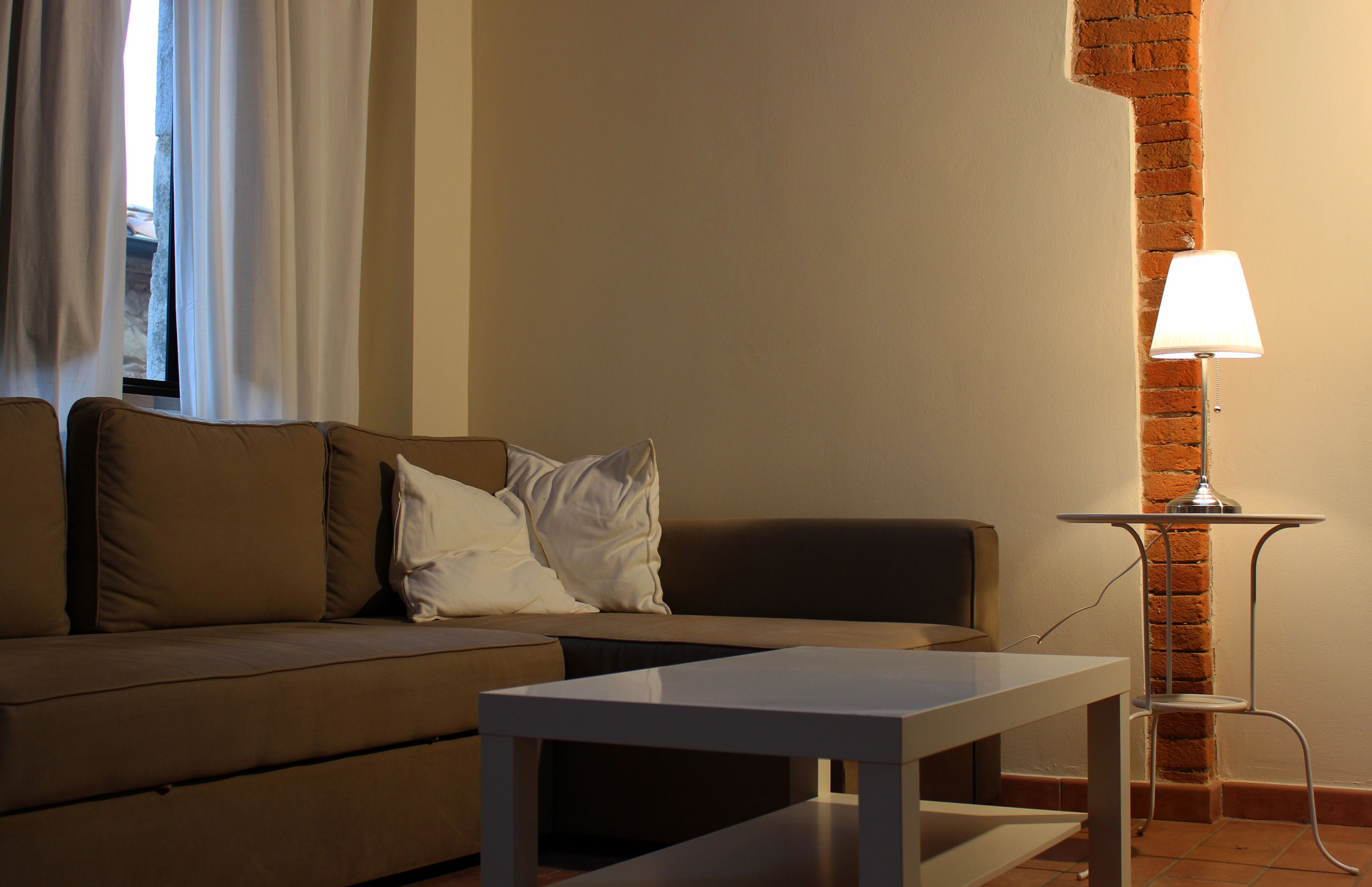 Ein Wohnzimmer mit einer Couch, einem Couchtisch, einer Lampe und einer Ziegelwand.