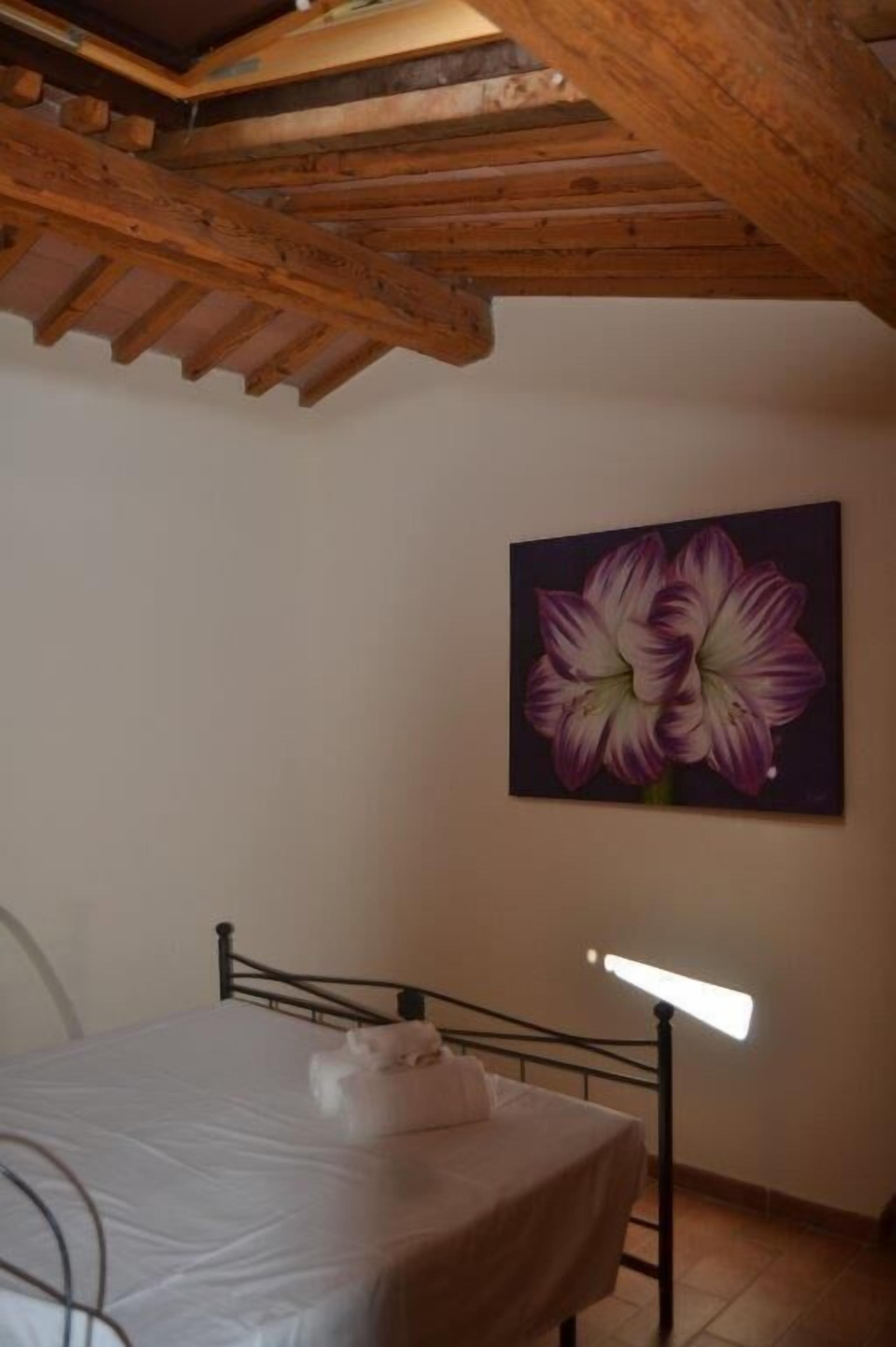 Un dormitorio con cama, techo con vigas de madera y un cuadro de flores en la pared.