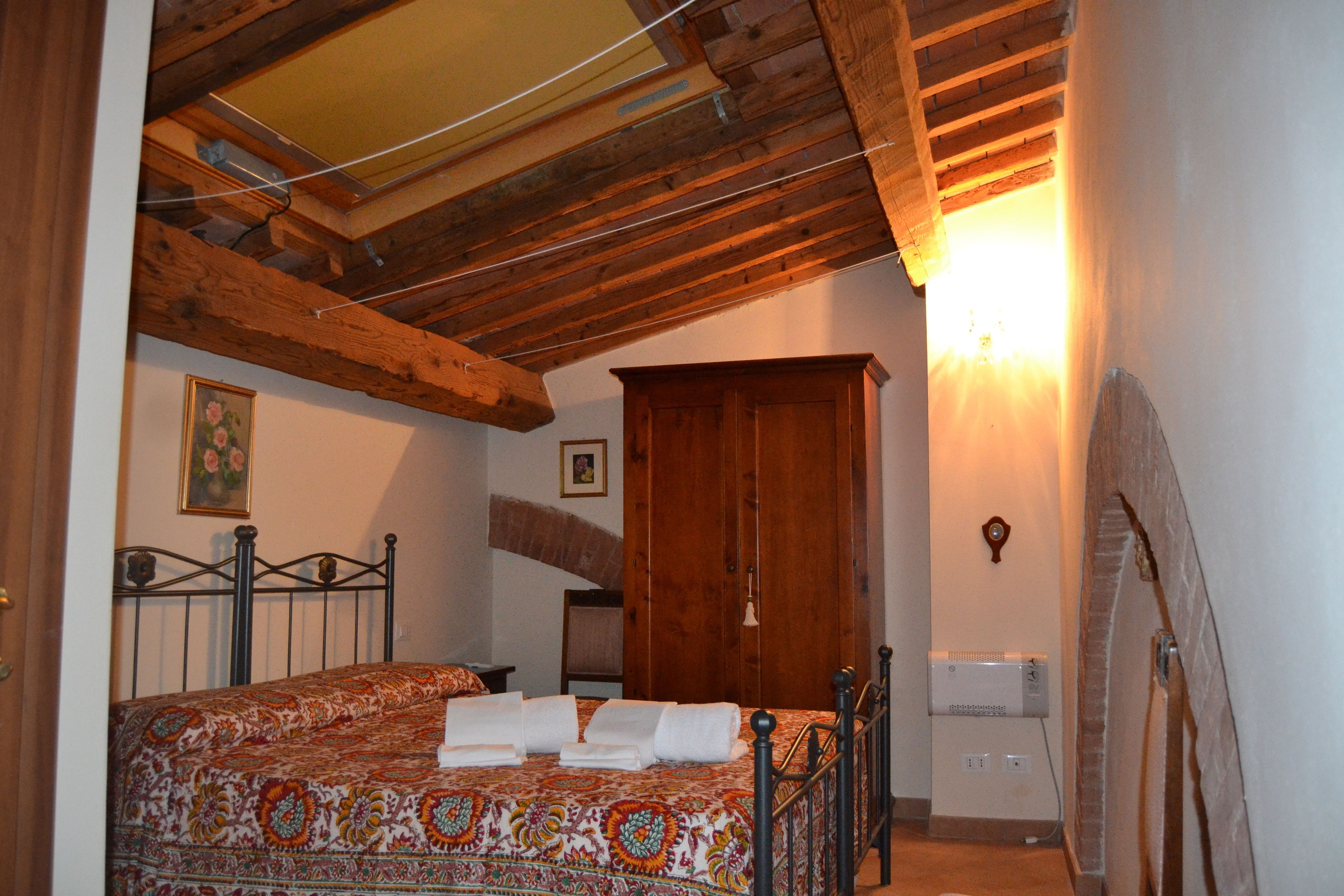 A bedroom with a bed, wooden beams, a wardrobe, and a radiator.