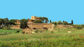 A historic building complex with multiple structures, including a prominent tower, surrounded by lush greenery and fields. - Antico Borgo Casalappi (Campiglia Marittima)