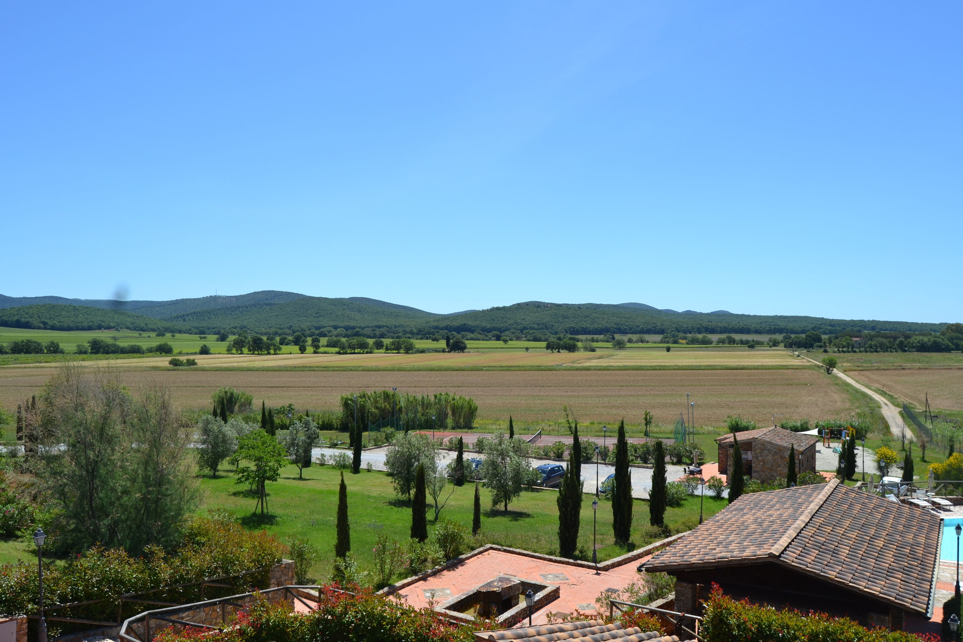Ländliche Landschaft mit Blick auf ein Haus mit Ziegeldach, umgeben von grünen Feldern und Bäumen.
