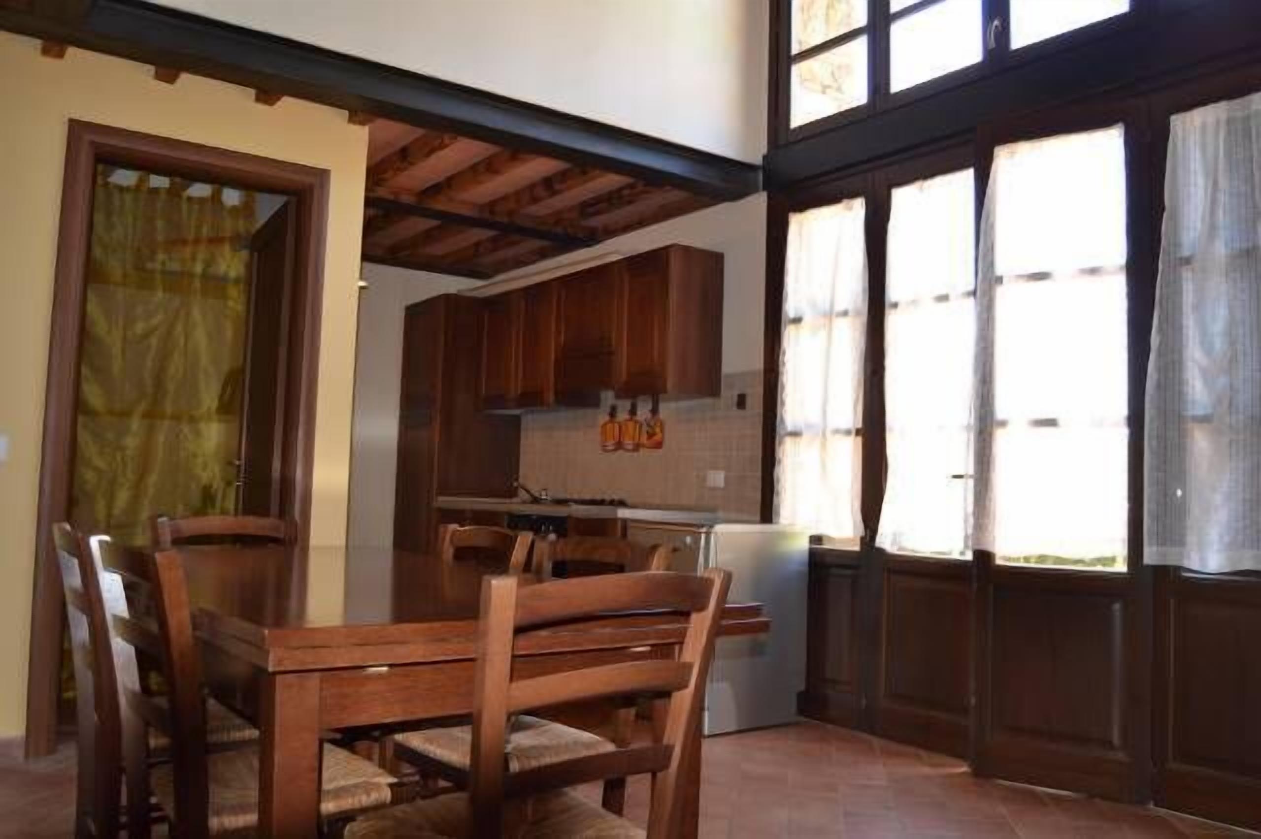Un coin repas avec des chaises et une table en bois, une cuisine avec des placards en bois et une fenêtre avec des rideaux.