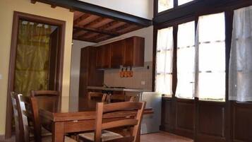 Un coin repas avec des chaises et une table en bois, une cuisine avec des placards en bois et une fenêtre avec des rideaux.