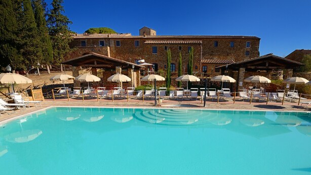 A pool area with lounge chairs and umbrellas, surrounded by stone buildings with a rustic appearance. - Antico Borgo Casalappi (Campiglia Marittima)