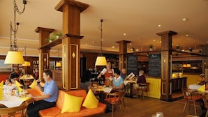 A restaurant with wooden furniture, yellow cushions, and hanging lamps. - Golfhotel Gutshof Penning (Rotthalmuenster)