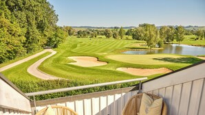 A balcony with wicker chairs and a table, overlooking a golf course and a lake. - Golfhotel Gutshof Penning (Rotthalmuenster)