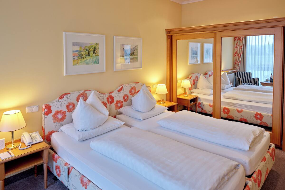 A hotel room with two beds, floral-patterned bedding, bedside lamps, a telephone, and framed artwork on the wall.