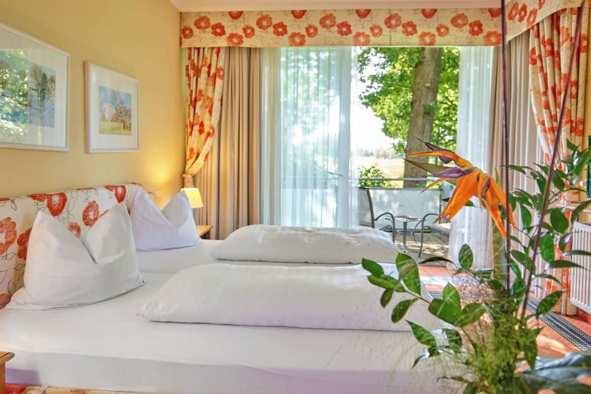 A hotel room with a bed, a sofa, a table, and a chair. There are curtains and a plant in the room.